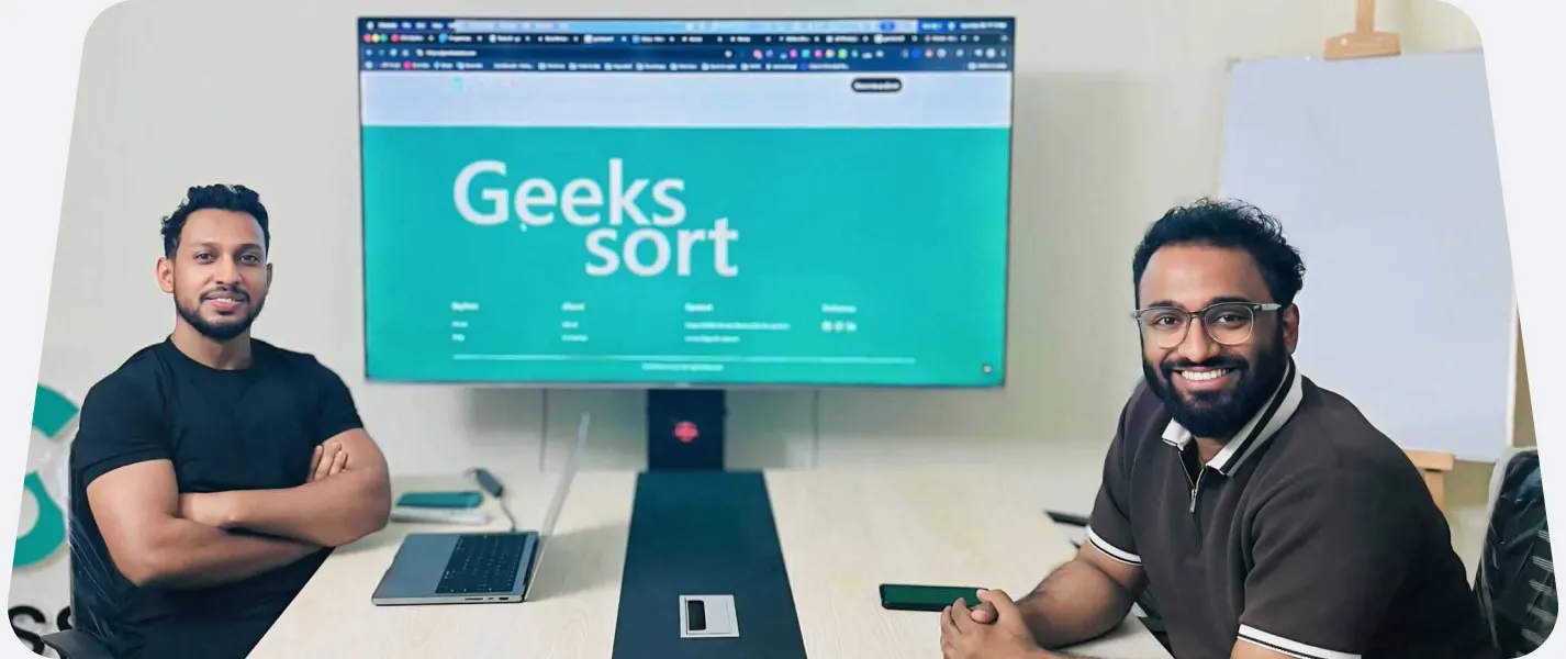 Two team members either side of a monitor showing the Geekssort mark