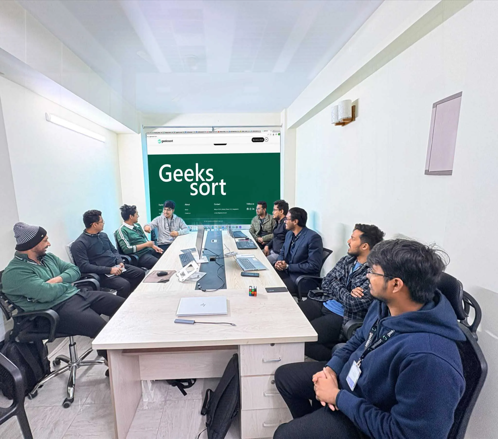 The team in a full-length meeting around the boardroom table, under the Geekssort sign.