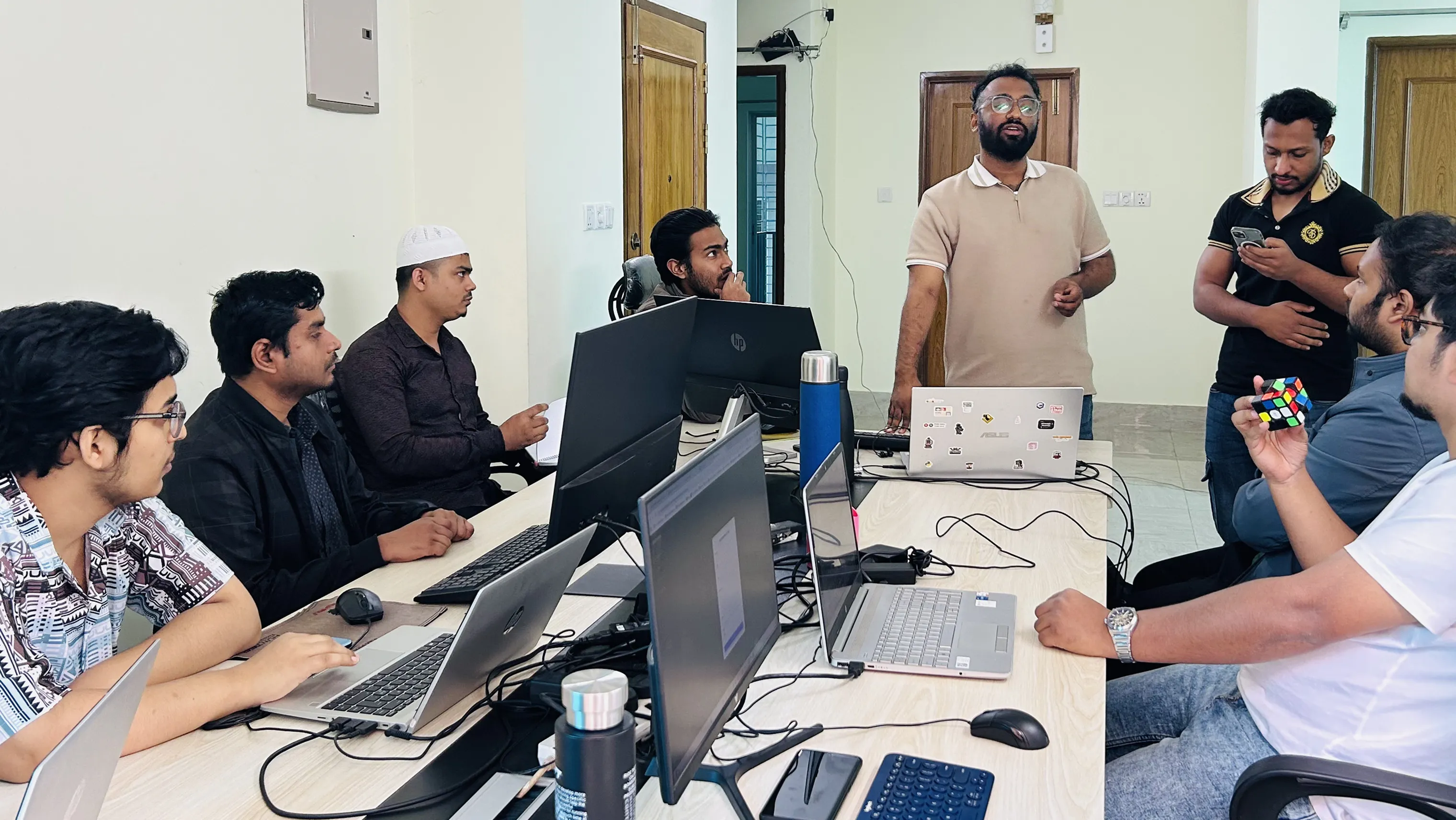 A team member presenting to the room beside a bench of open laptops.