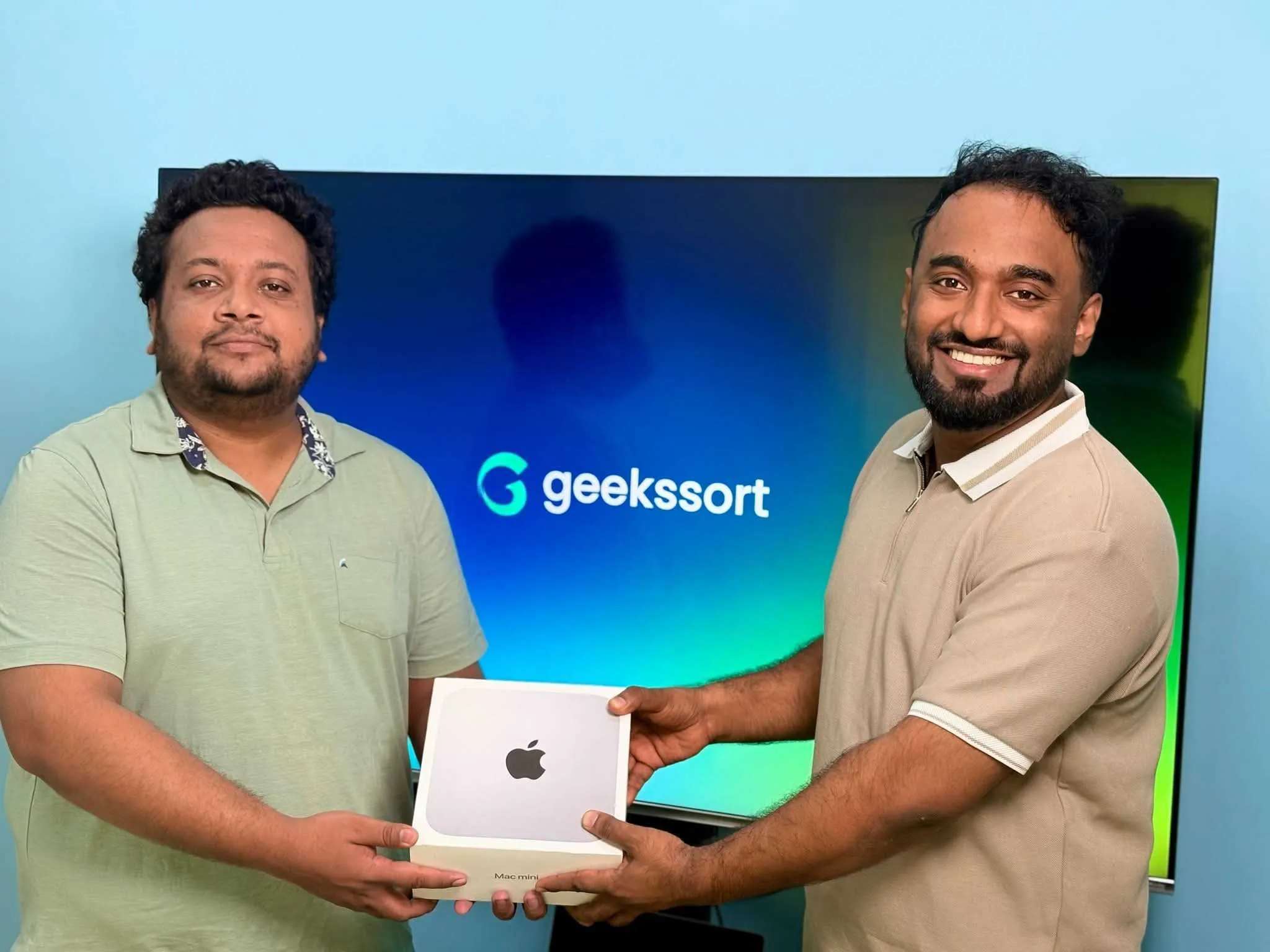 Two colleagues holding a new laptop in front of a screen showing the Geekssort logo.